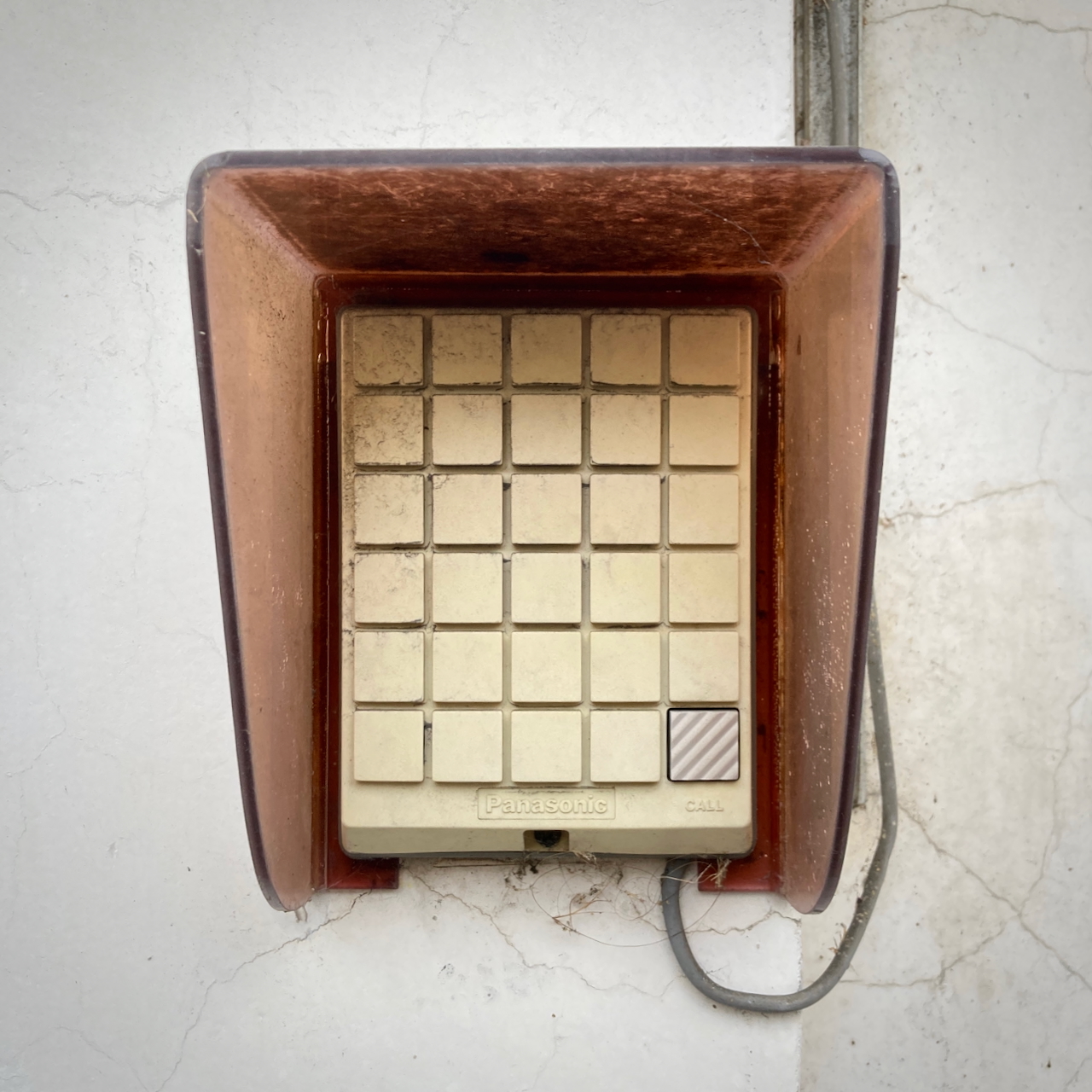 A photograph of a beige control panel, attached to a wall. There's a grid of 5 × 6 buttons – except they're not buttons, they're just a mold where the buttons would be. Only the lower right of these 30 potential buttons is actually a button, and it's very lightly embossed with the word 'CALL'.